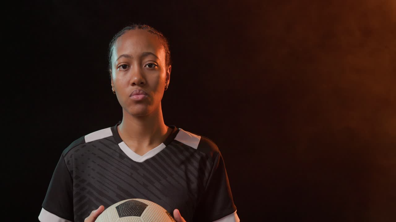 La telecamera zooma su una calciatrice africana adulta che sistema il pallone per un ritratto, con un alone arancione luminoso