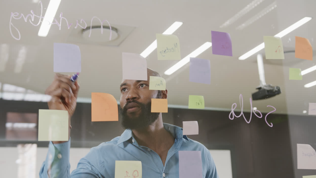 African american businessman brainstorming, making notes on glass wall in office in slow motion