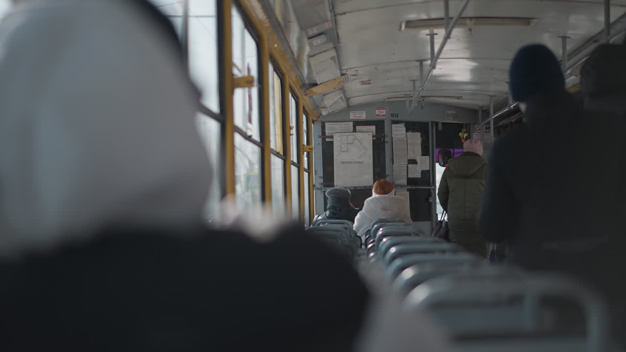 back view of winter passengers inside train moving to door as carriage slows for stop, figures stand from seats and step down aisle, cold light through windows and yellow frames, urban transit mood