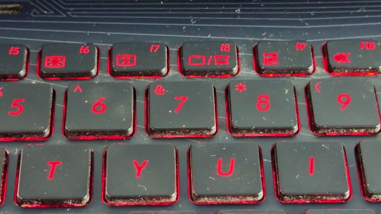 Hånd, der taster på bærbar computers tastatur, finger trykker på taster i svagt lys med glødende rødt baggrundslys