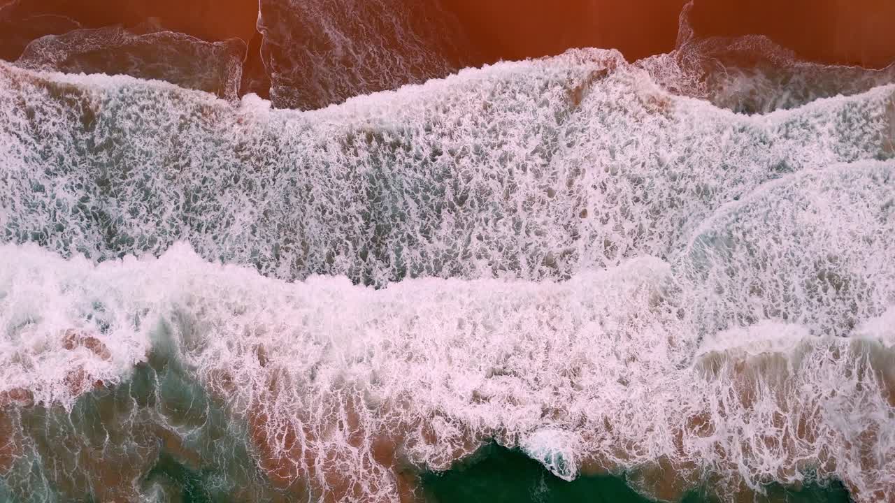 Aerial shot of a wave's frothy crest breaking along the shoreline, The sea's lace-like foam meeting the beach