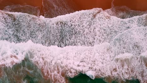 Aerial-shot-of-a-wave's-frothy-crest-breaking-along-the-shoreline,-The-sea's-lace-like-foam-meeting-the-beach