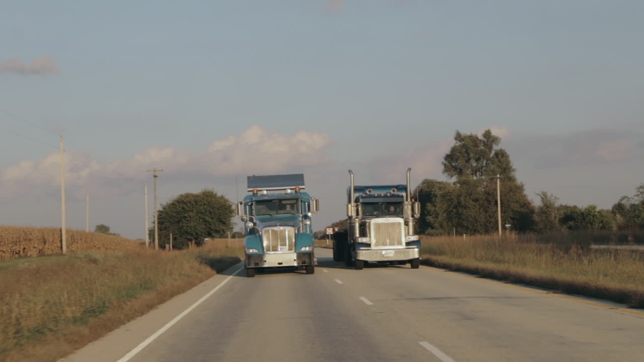 Two Peterbilt semi eighteen wheeler trucks driving down the highway in evening sun side by side