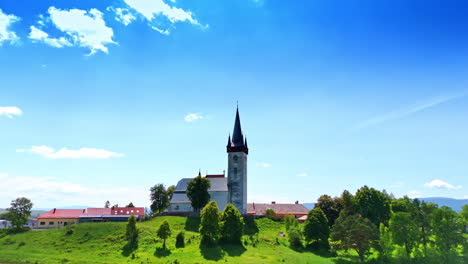 church on hilltop in summer daylight. a historic church stands on a grassy hill with trees, surrounded by colorful buildings under a bright blue sky