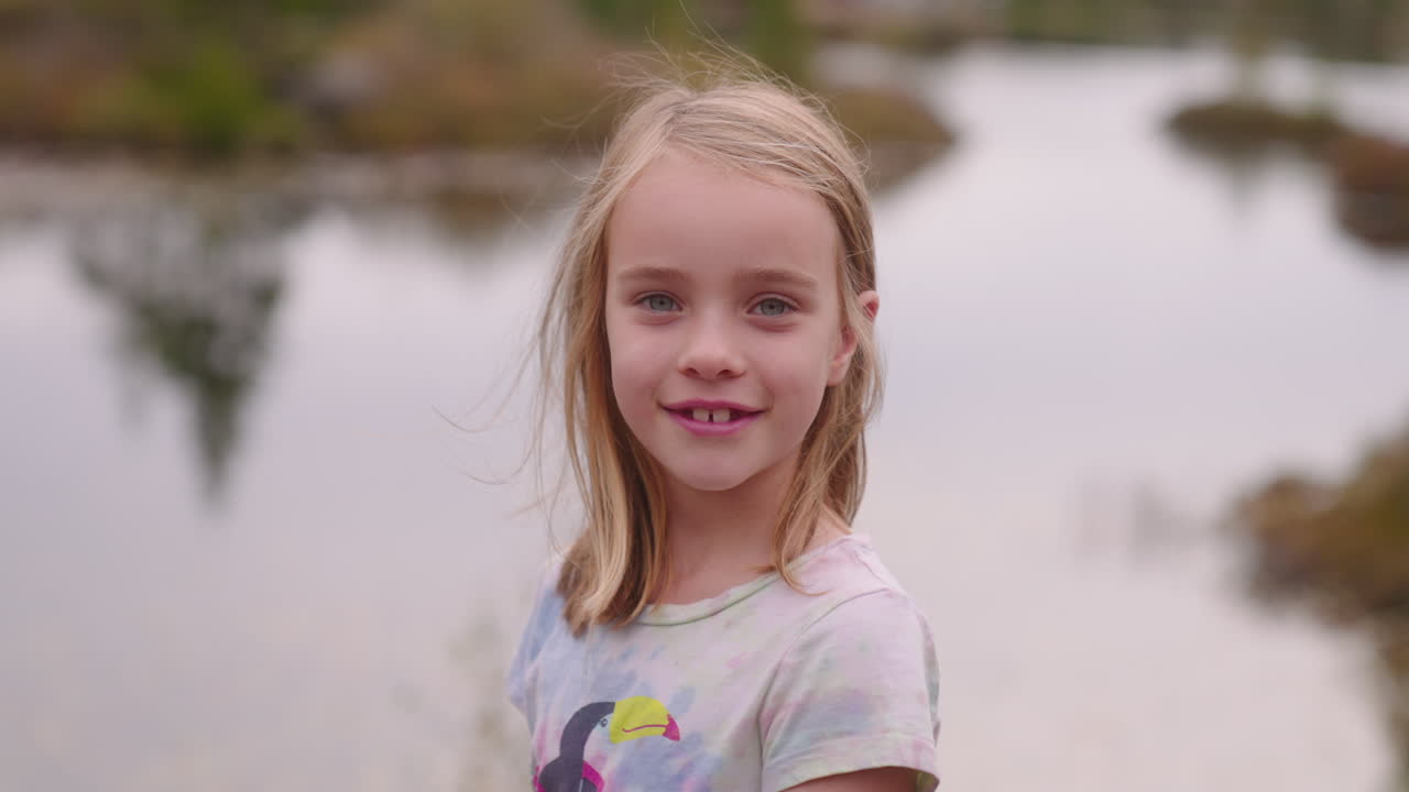 Uma linda garotinha olha para um lago, se vira e sorri para a câmera