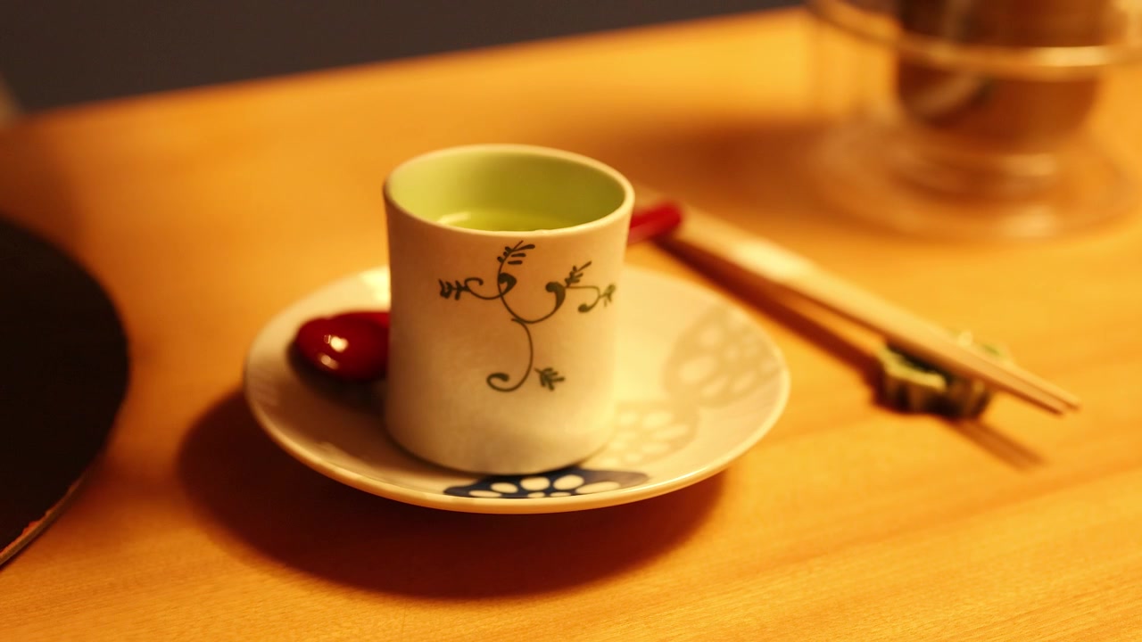 A hand lifts the lid of a ceramic cup to reveal Japanese steamed egg custard