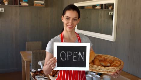 retrato de una panadera con baguettes y un cartel abierto