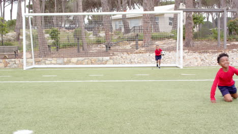 multiracial boys playing soccer on field, one running joyfully, another celebrating goal