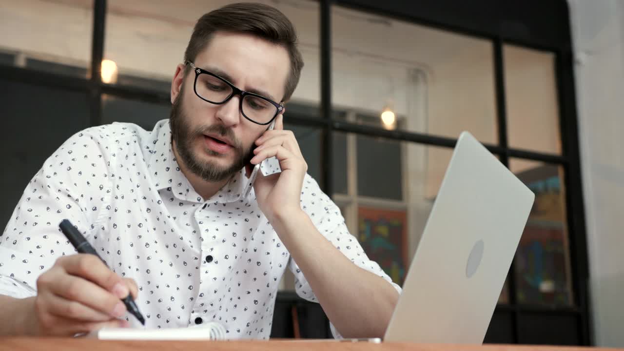 hombre hablando en teléfono inteligente y escribiendo en la oficina