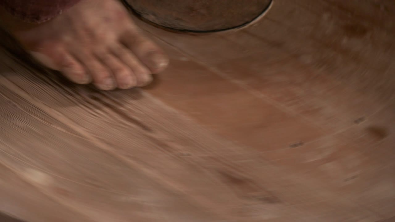 el alfarero gira la rueda de madera de la rueda del alfarero con sus pies