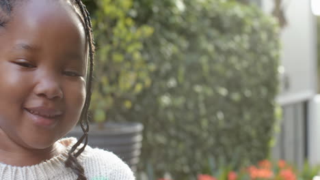 Portrait-of-african-american-girl-with-braided-hair-smiling-in-sunny-garden,-copy-space,-slow-motion