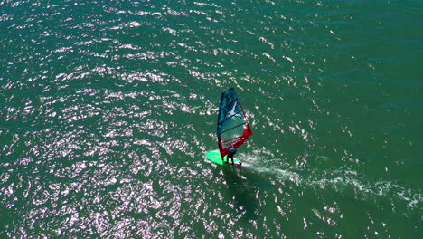 Windsurfista-Surfeando-Y-Tratando-De-Encontrar-Condiciones-De-Viento-Perfectas,-Tiro-Aéreo