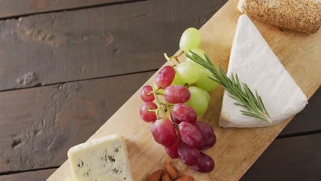 video of cheeses, grapes, nuts and rosemary on chopping board, on wooden table with copy space