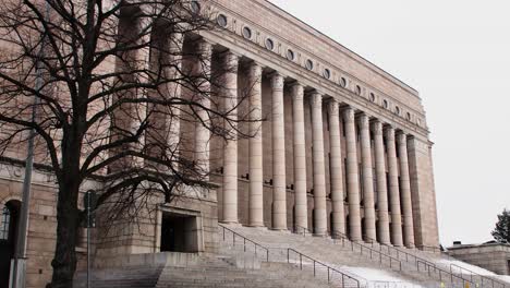 tree branches framing the imposing facade of helsinki's parliament house, overcast sky