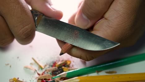 imágenes de manos afilando lentamente un lápiz y algunos lápices de colores con un cuchillo afilado