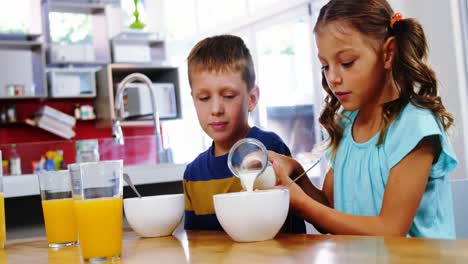 Girl-pouring-milk-into-cereal-bowl-in-kitchen