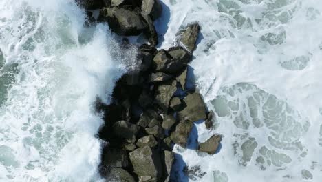 overhead drone shot of sea waves break the stones slow motion