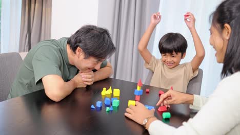 a family joyfully engages in a playful educational activity using colorful shapes at a table in a bright room