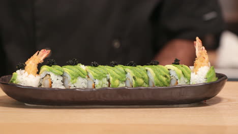 chef putting roe on top of shrimp tempura sushi roll with avocado slices using a teaspoon - close up, panning shot