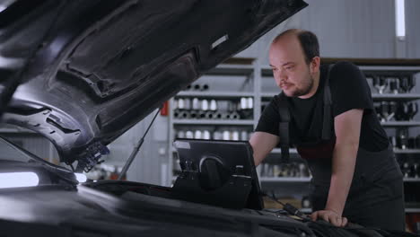 man mechanic at the hood of a car with a tablet diagnoses all systems and searches for malfunctions