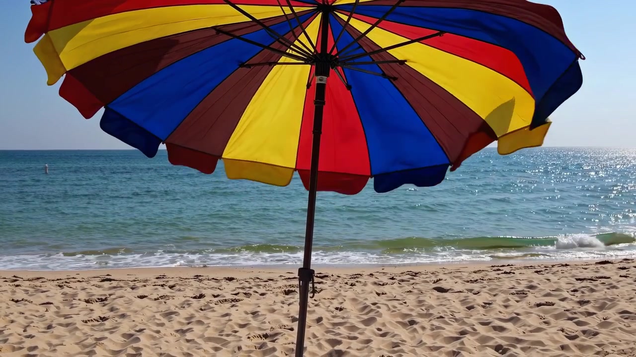 Ombrellone da spiaggia colorato su una riva sabbiosa con dolci onde dell'oceano