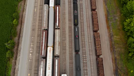 4k aerial view of multiple trains sitting at a train station while revealing a long straight railway with multiple tracks ahead next to a small town