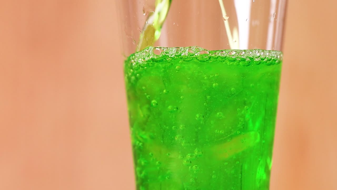 Um refrigerante verde brilhante preenche um copo transparente contra um fundo de madeira quente