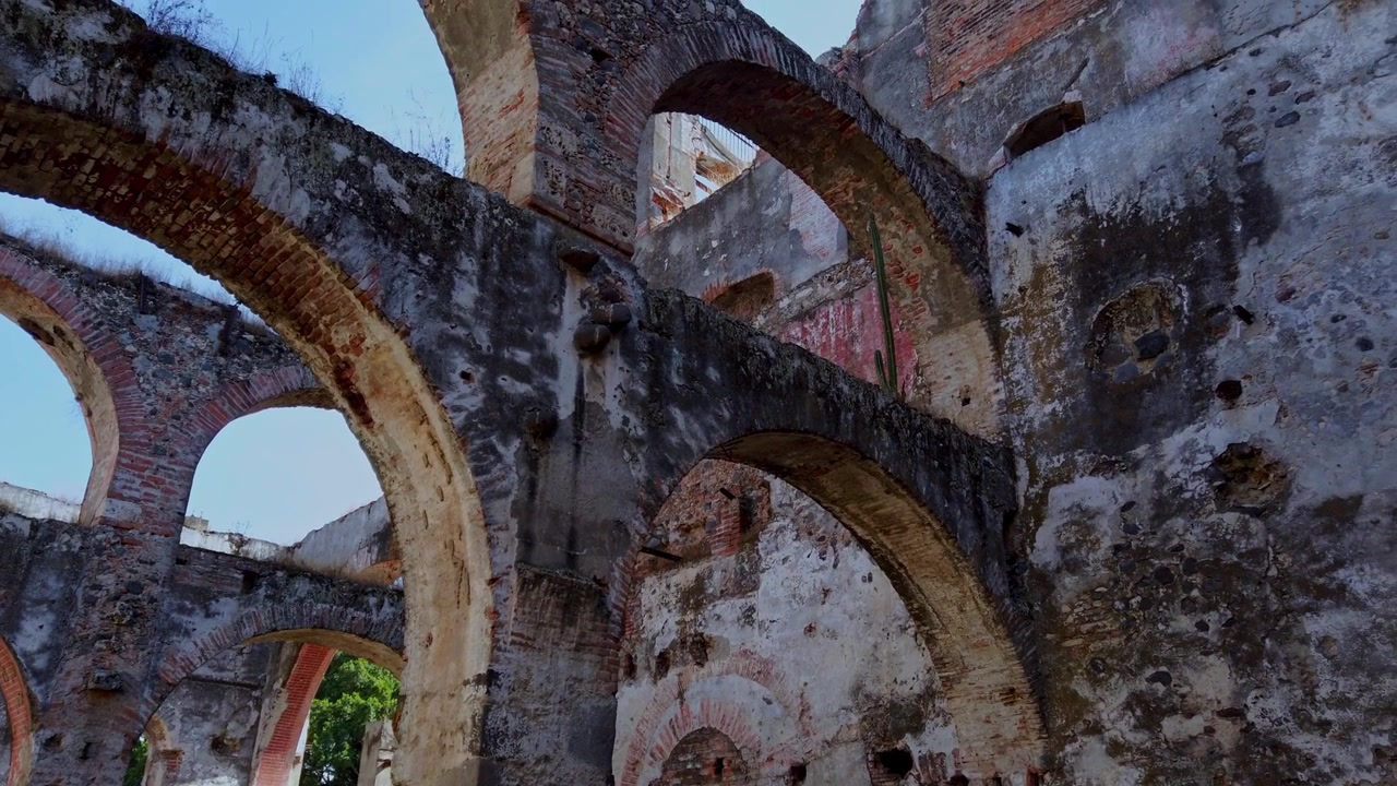 Pemandangan reruntuhan hacienda tua dengan lengkungan bata besar dan dinding yang menua di bawah langit cerah, menampilkan tekstur kuat dan detail arsitektur yang menunjukkan sejarah serta warisan budaya.