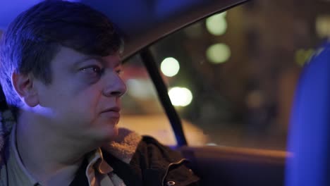 slow motion close up of young handsome businessman looking outside during traveling in a modern car with a driver in center of the city by the night. city lights