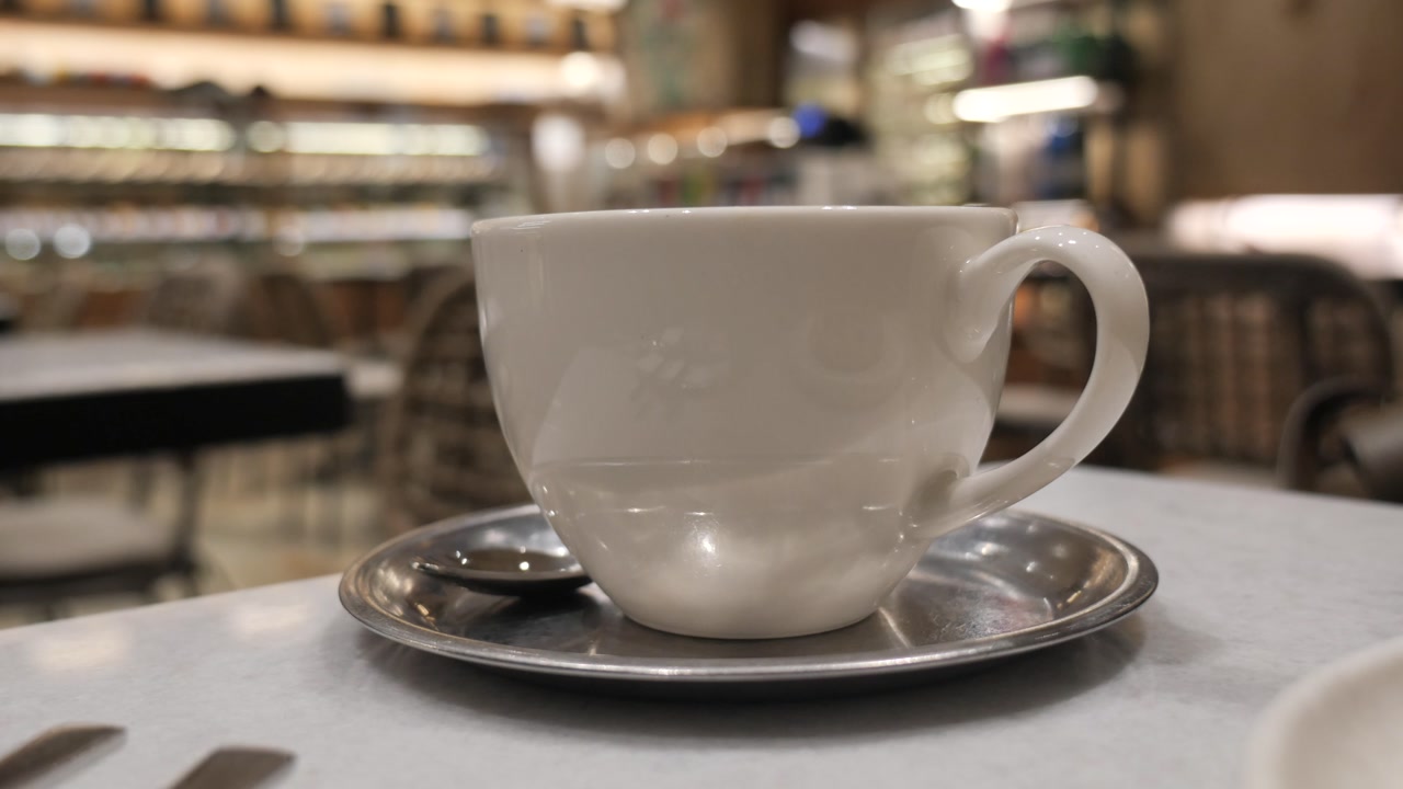 Hand Lifting White Coffee Cup from Table in Cafe