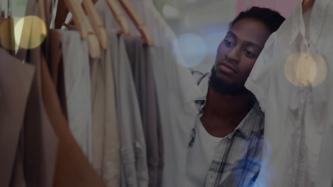 Animation of bokeh lights over african american man tidying clothes display in shop