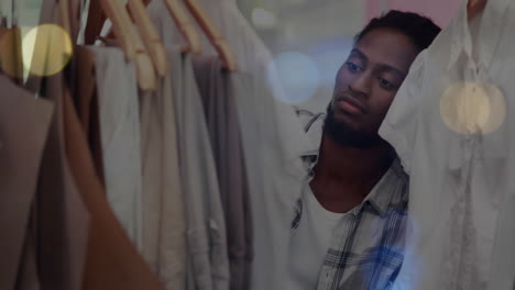 animation of bokeh lights over african american man tidying clothes display in shop