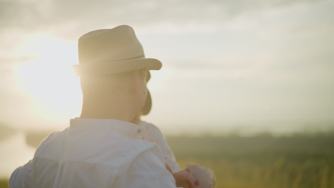 A close-up of a joyful husband and wife dancing together at sunset, both dressed in white shirts and hats. The warm, golden light highlights their happy expressions
