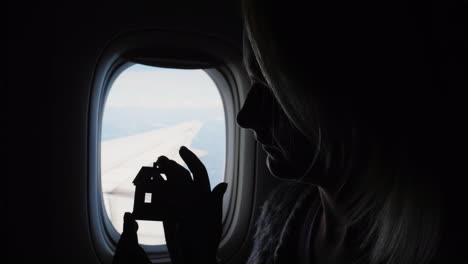 woman holds house figurine by airplane window