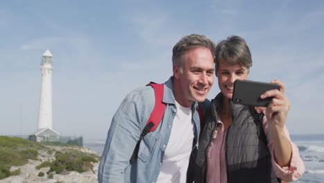 caucasian couple enjoying free time by sea on sunny day taking photo with phone