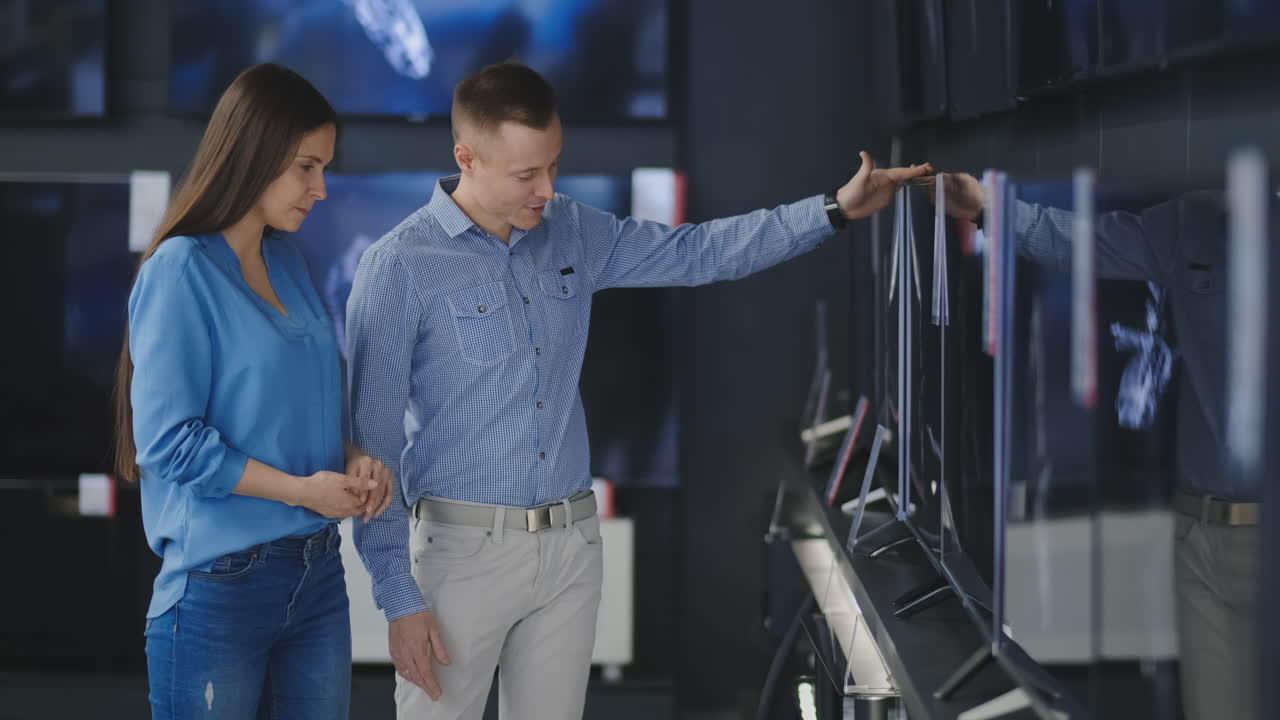 Couple in shopping. They are looking for new tv. They are pointing fingers at tv. Shallow depth of field. 4K UHD