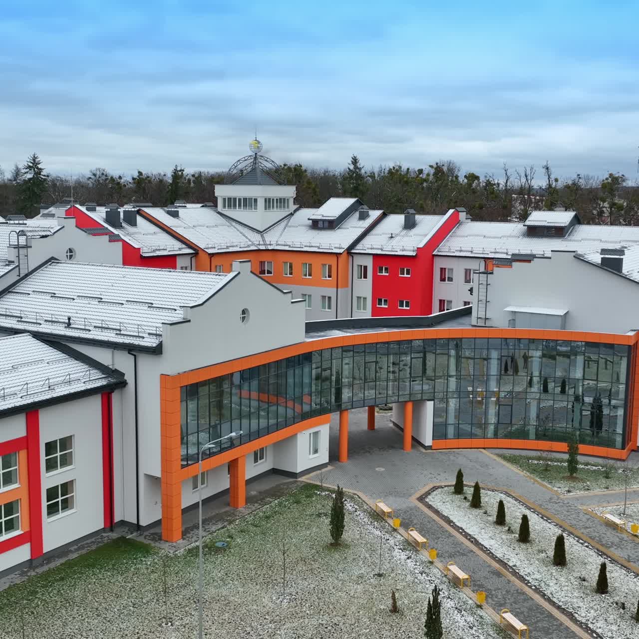 Modern design of the building with the unusual shape. Bright colored walls and mirrored windows in the building. Lawn with young trees at the forefront
