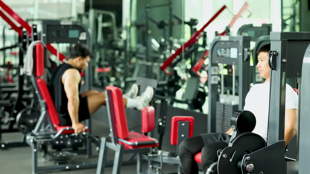 Two individuals perform leg press exercises in a well-lit gym, focusing on strength training with modern equipment