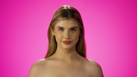 medium shot of a pretty blonde woman with beautiful red lips who is revealed by the blur and directs a friendly look at the camera against pink background in slow motion