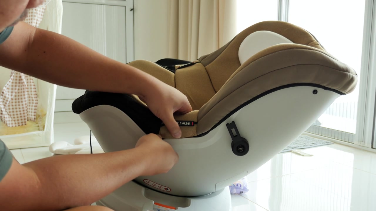 Hands meticulously secure an infant car seat in a well-lit room. Useful for parenting guides or safety tutorials.