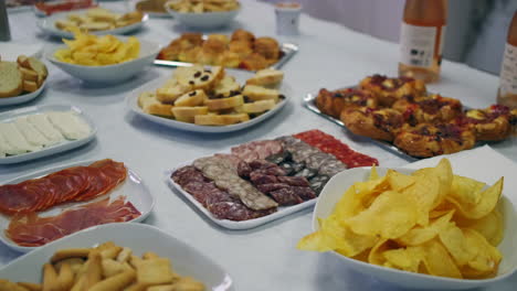 A-table-full-of-sliced-meats,-cheeses,-potato-chips-and-wine