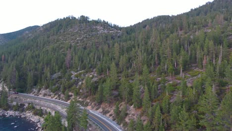 Panning-View-of-Alpenglow-Over-Pristine-Calm-Waters-and-Pine-Tree-Forest-in-Mountains-of-Lake-Tahoe-In-California-at-Sunset---aerial-drone-shot