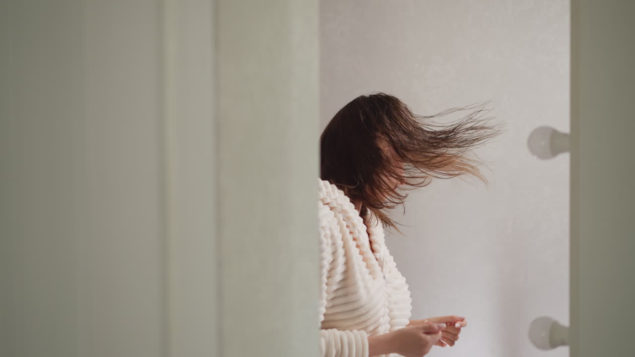 화장실에서 거울을 반사하는 음악에 여성이 움직입니다. 은 머리카락을 가진 젊은 갈색 여성은 샤워 후 음악과 함께 느린 동작을 즐기고 있습니다.