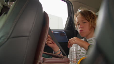 boy drinking water and holding phone in car