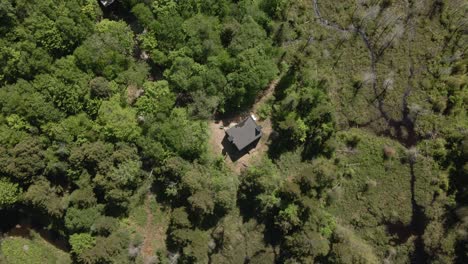 Bird's-Eye-View-Of-The-Small-Cabin-House-On-The-Midst-Of-The-Green-Forest