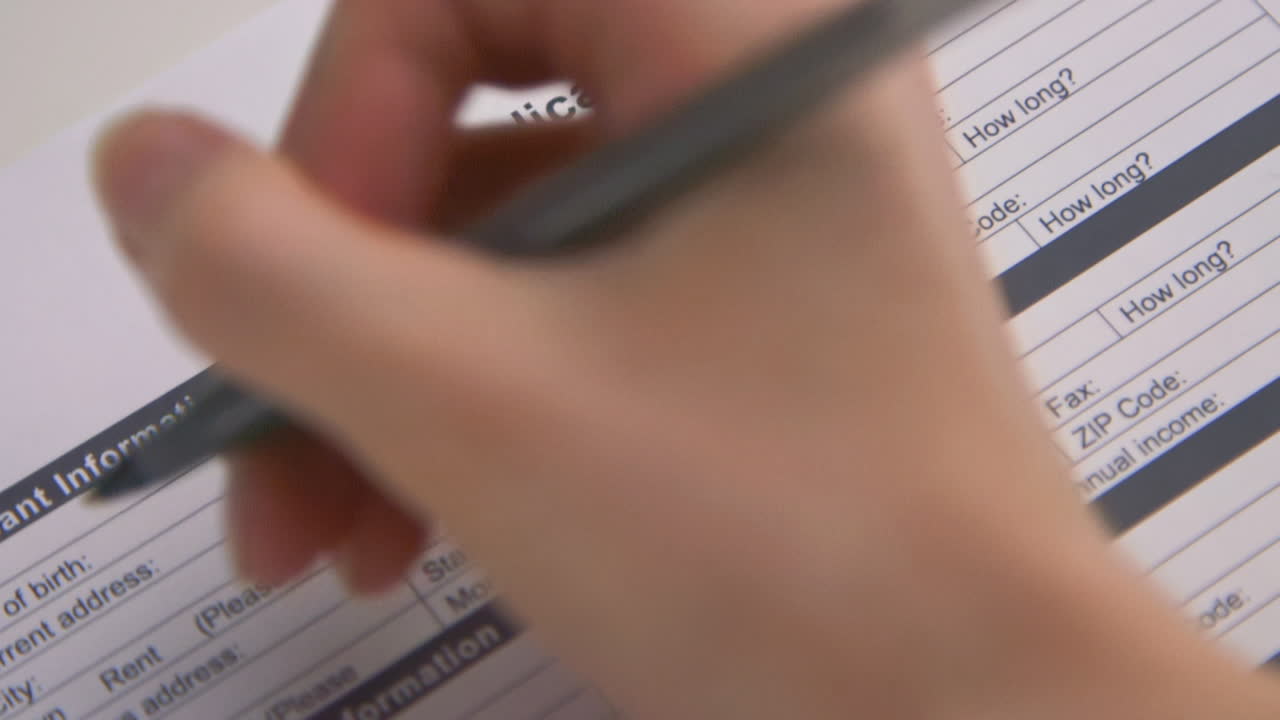 A caucasian woman's hand fills out a Rental Application