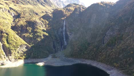 Lac-d'Oô-waterfall-at-the-artificial-lake-in-the-French-Pyrenees-created-by-the-runoff-of-Lake-d'Espingo,-Aerial-approach-shot