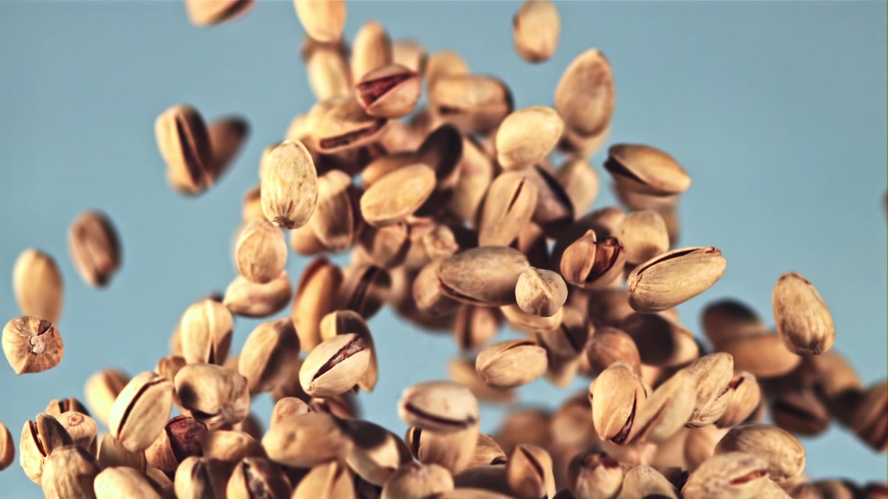 Pistachios Falling and Bouncing in Slow Motion Against a Blue Background