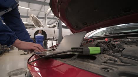 computer diagnostics of cars, young mechanic specialist male uses laptop technology while repairing vehicle with open hood at service station