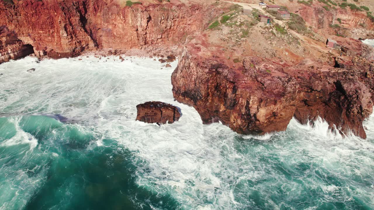 Aerial 4k drone circle view of large crashing waves at rugged cliff coastline near Bordeira in the Algarve region of Portugal